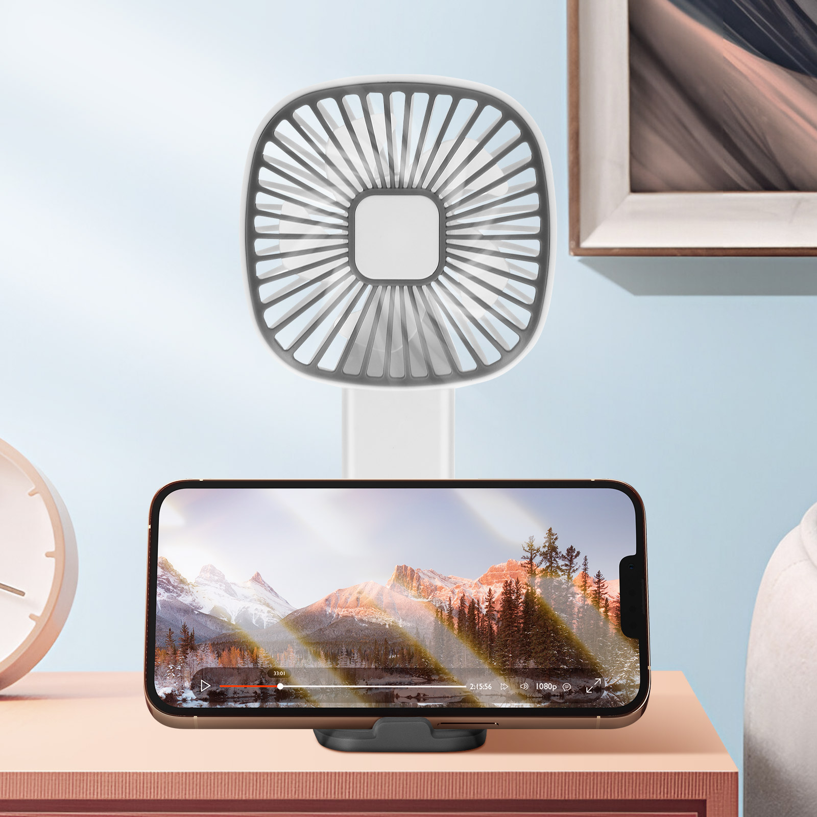 Ein Tischventilator steht hinter einem Smartphone, das ein Bergpanorama zeigt.