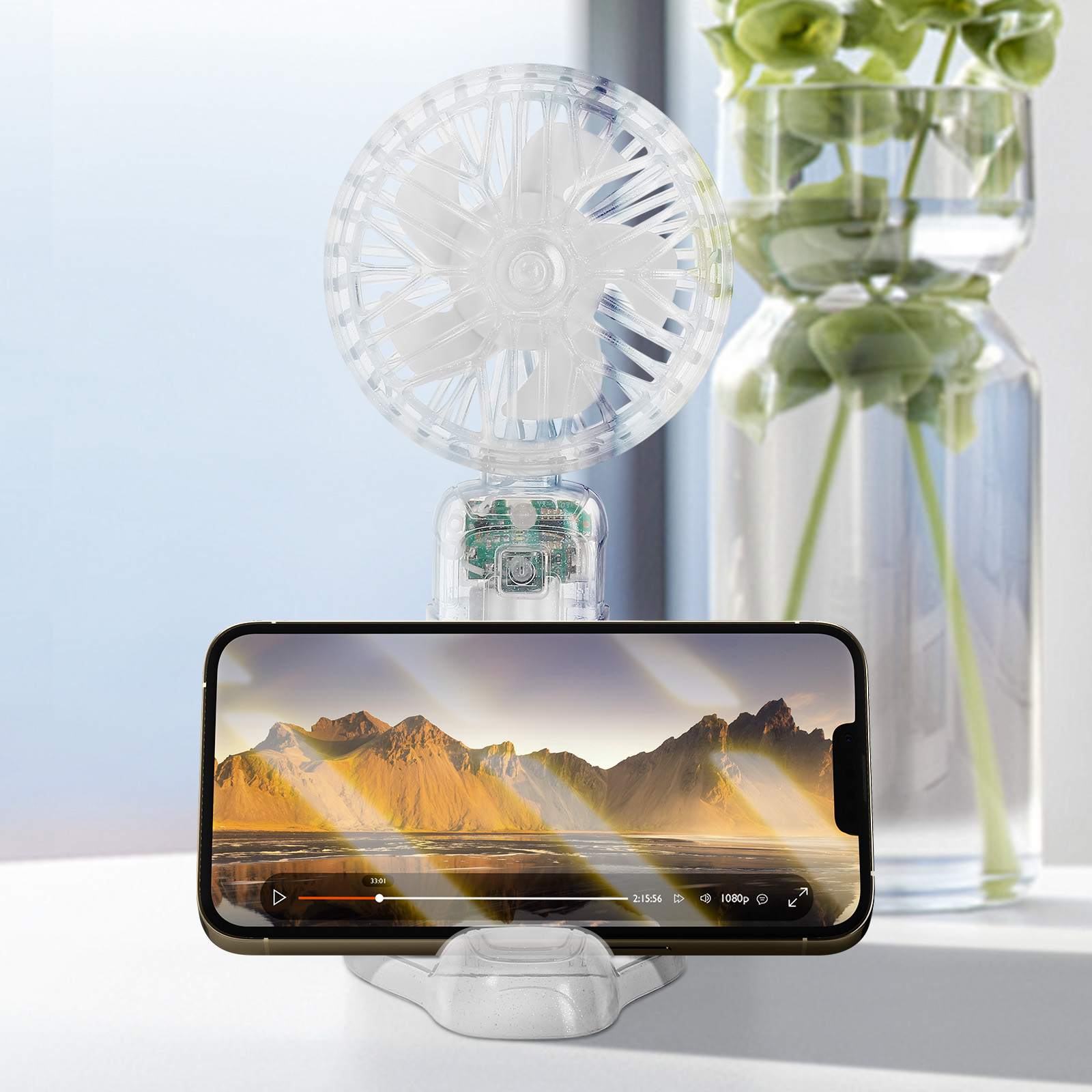 Ein durchsichtiger Ventilator steht hinter einem Smartphone, das eine Berglandschaft zeigt.