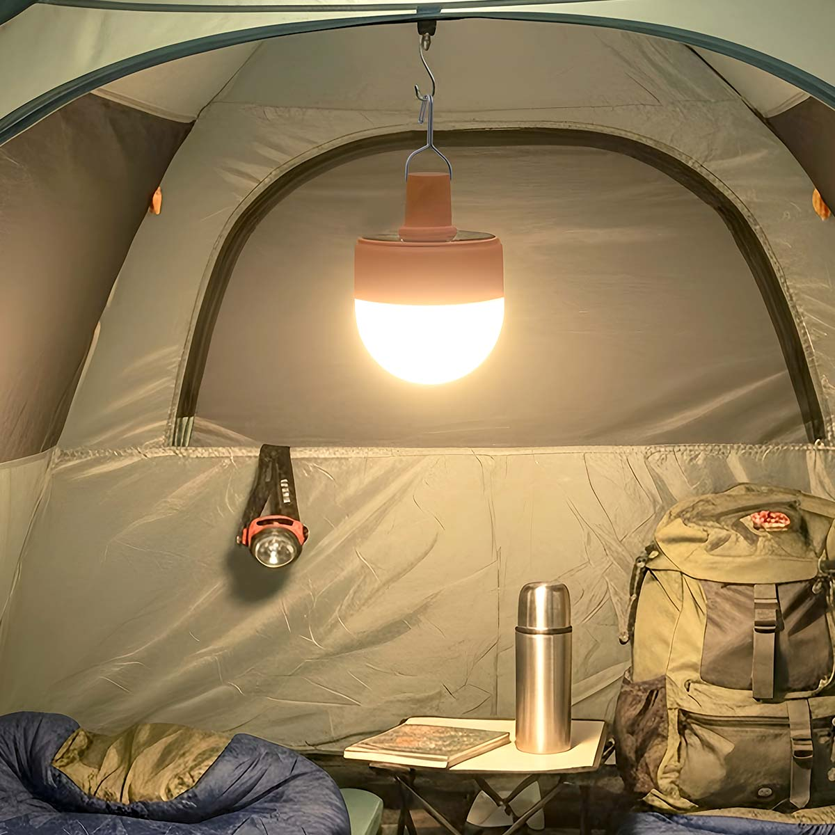 Una linterna de camping brillante cuelga dentro de una tienda sobre una bolsa, un termo y un libro.