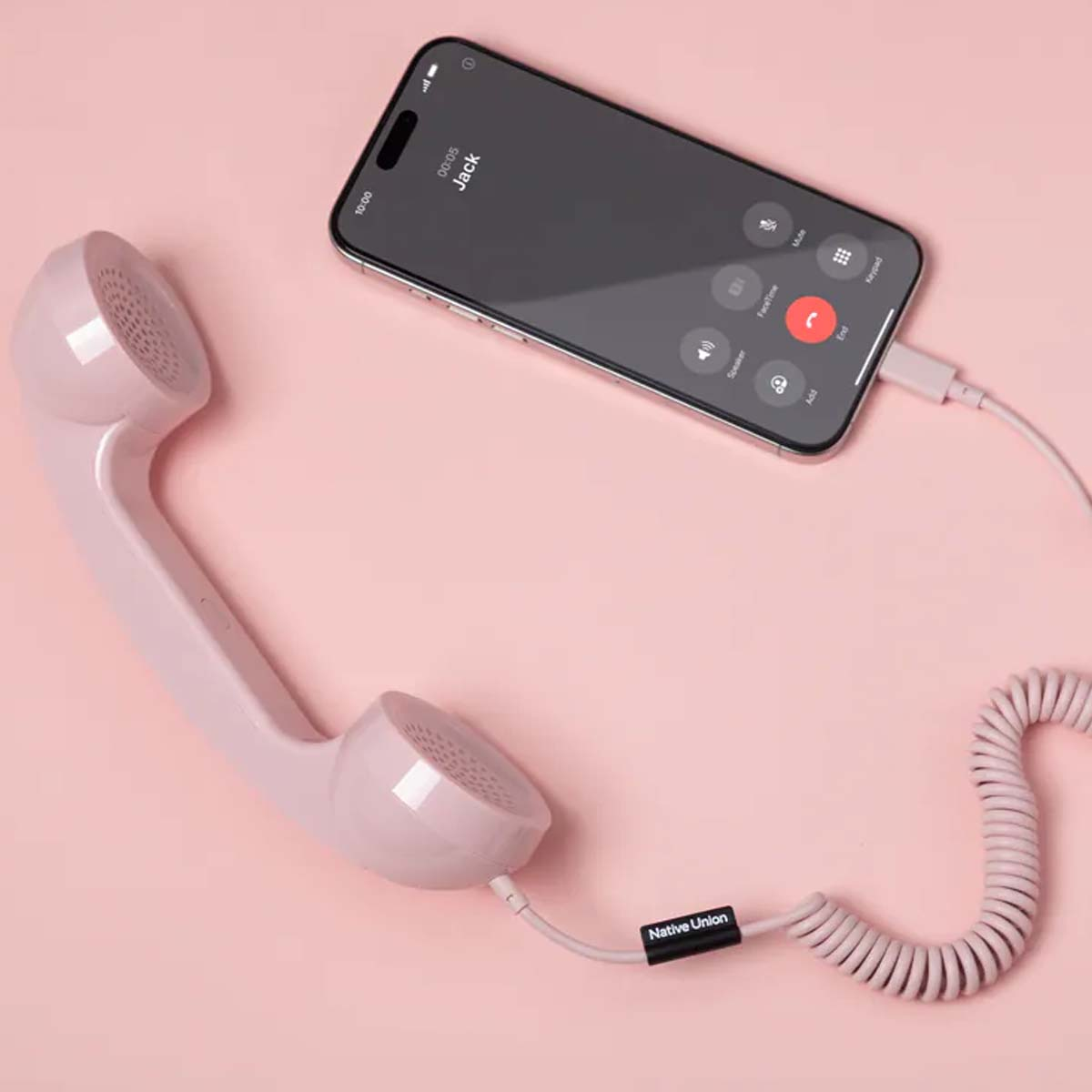 Una cornetta retrò rosa è collegata a un iPhone che mostra una chiamata attiva.