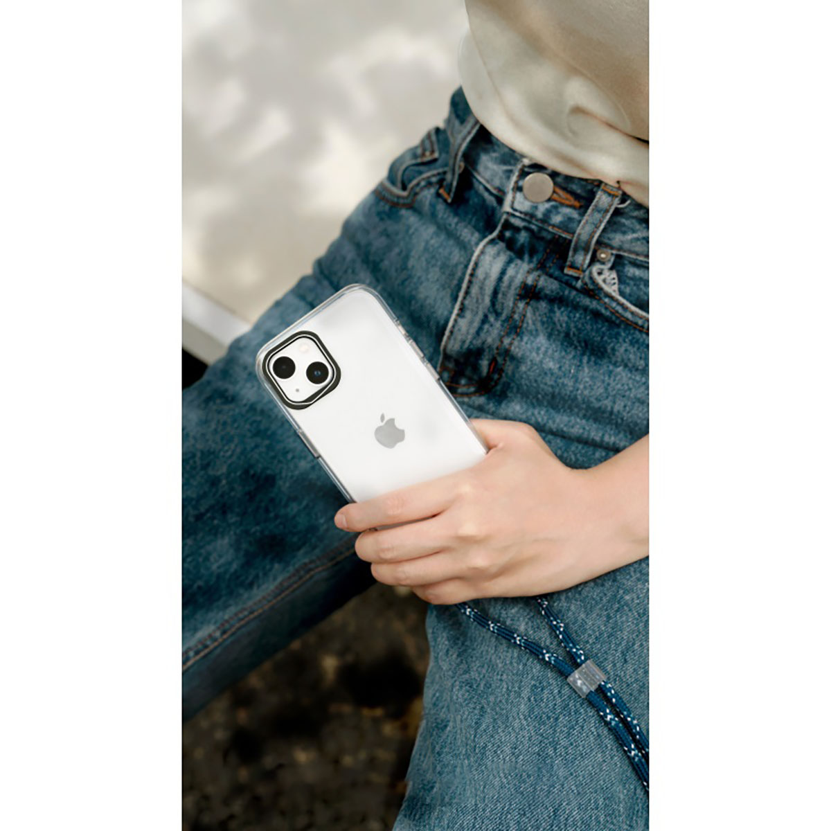 Eine Person hält ein iPhone mit Hülle und Lanyard in blauen Jeans.