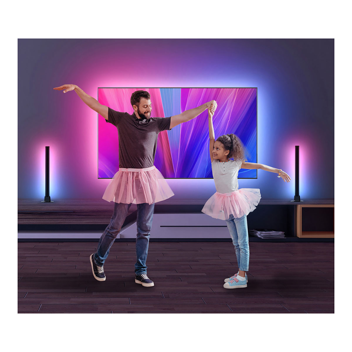 Mann und Kind tanzen Ballett vor einem beleuchteten Fernseher.