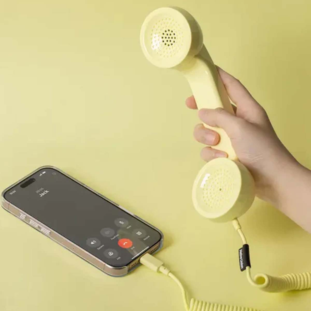 Una mano tiene una cornetta gialla collegata a uno smartphone.