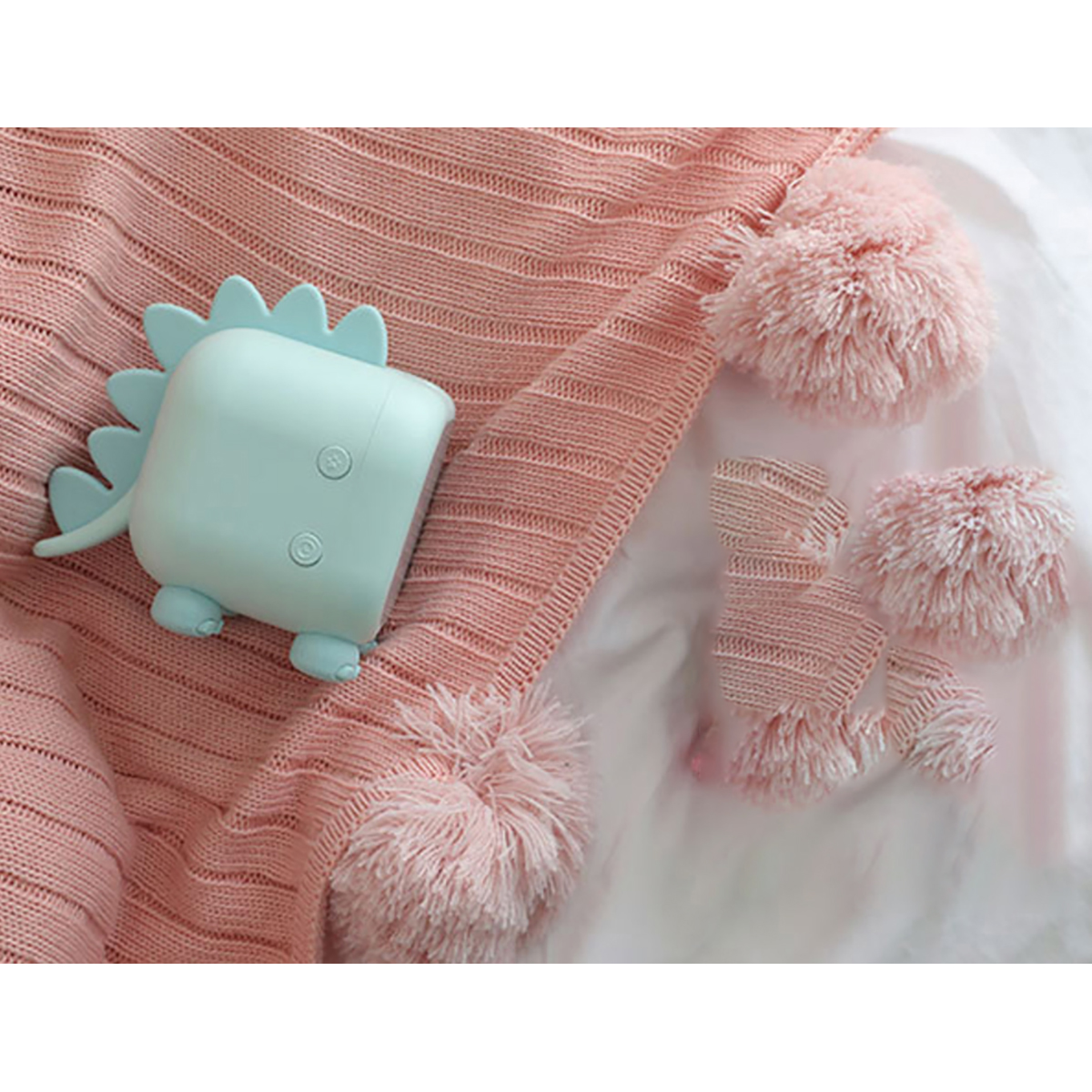 Un désodorisant dinosaure vert clair repose sur une couverture rose à pompons.