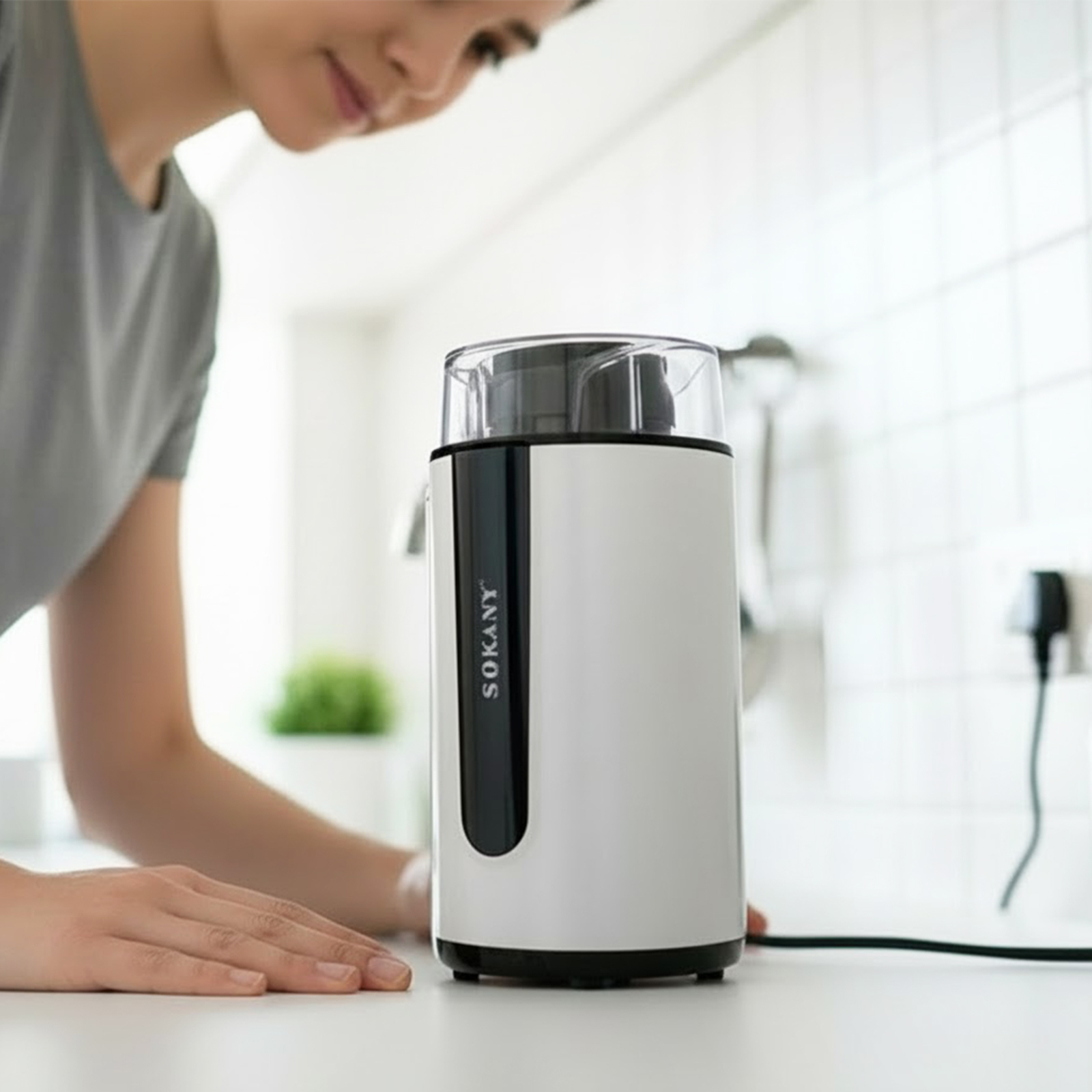 Eine Person benutzt einen weißen Kaffeemühle mit transparentem Deckel.