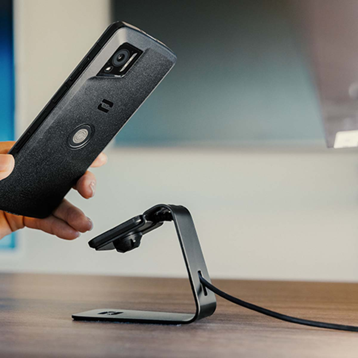 Una mano tiene uno smartphone sopra un supporto nero con un cavo.