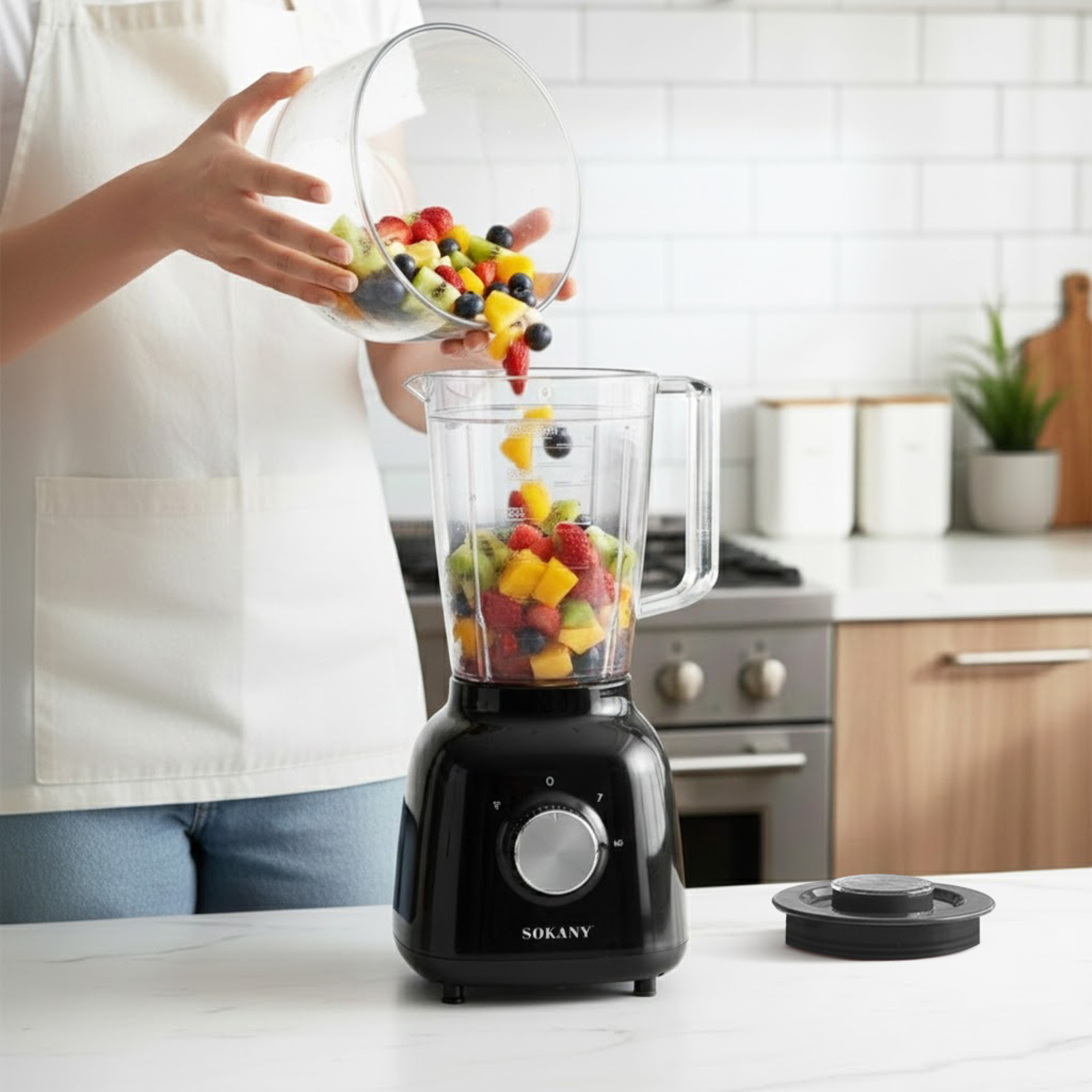 Fruta vertiéndose en una licuadora negra. Cocina al fondo.