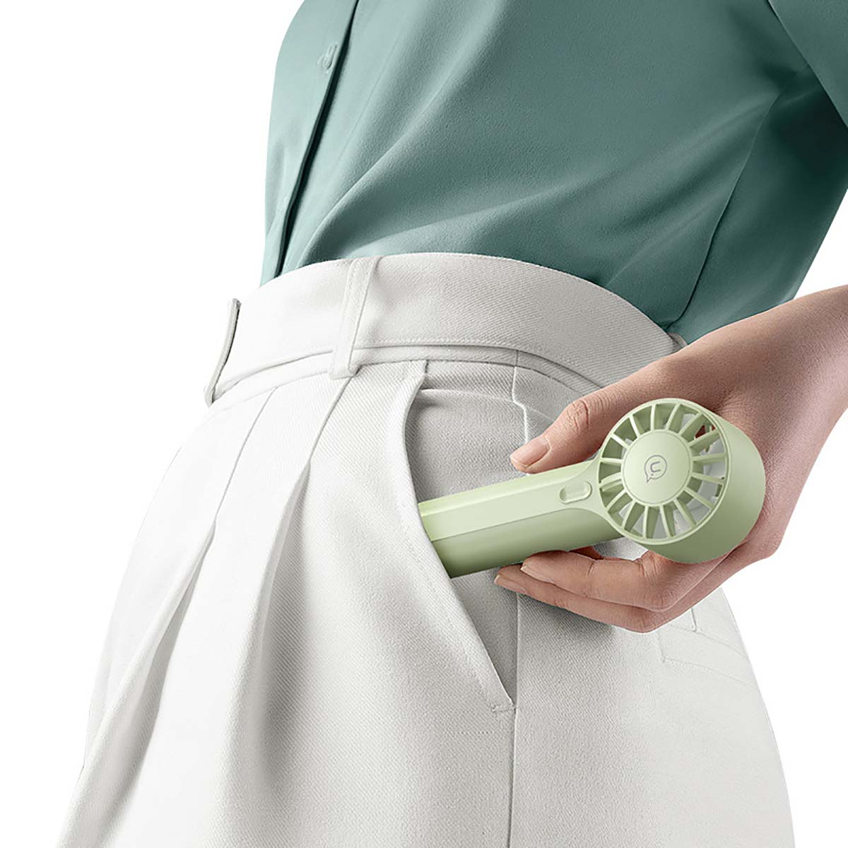 Una mano guarda un pequeño ventilador verde claro en un bolsillo blanco.