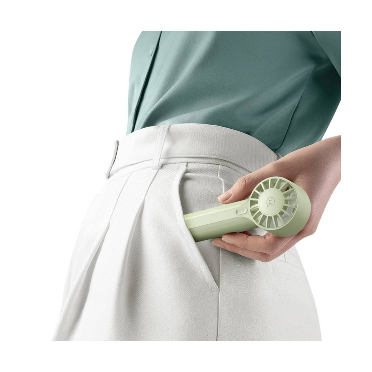Una mano guarda un pequeño ventilador verde claro en el bolsillo de un pantalón blanco.