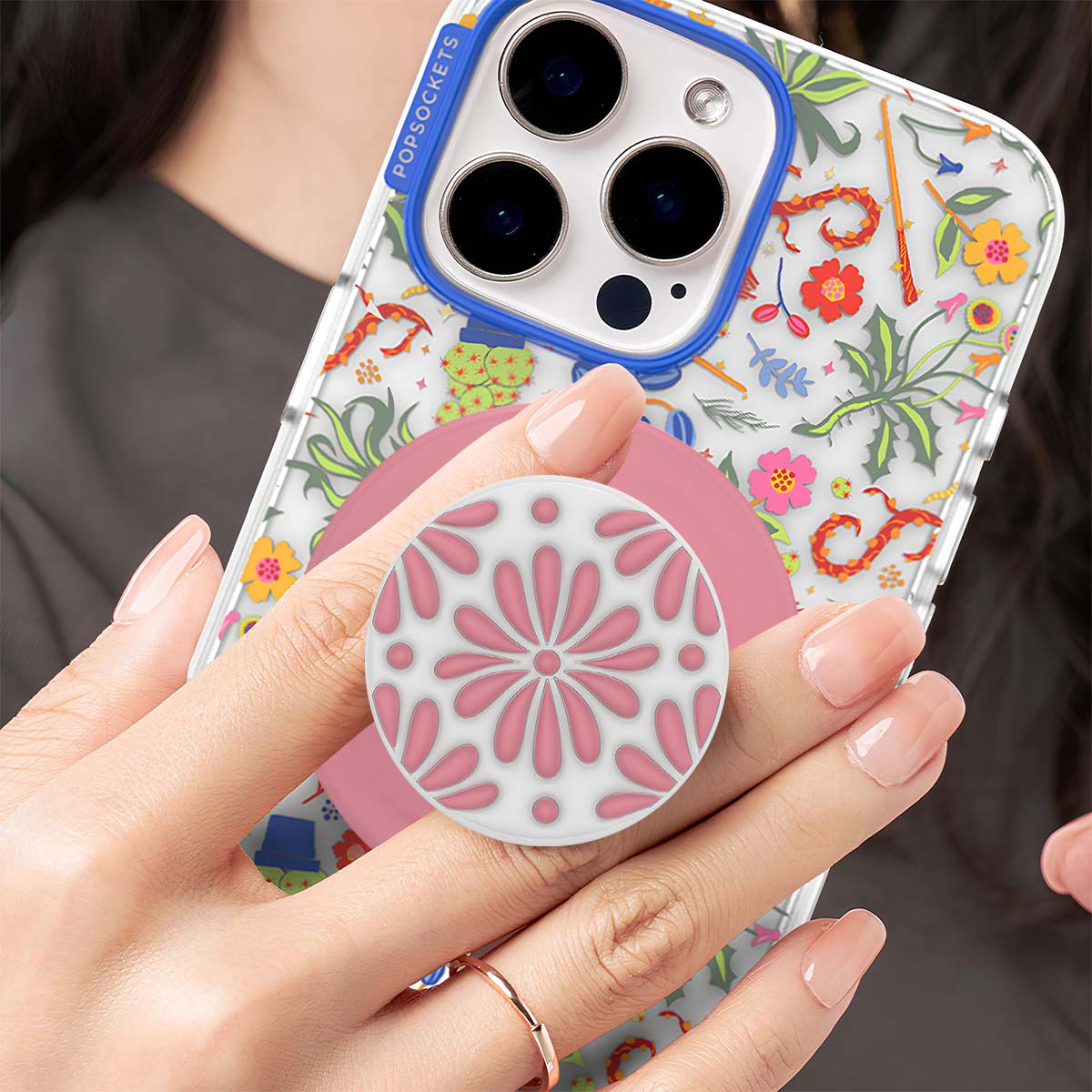 Una mano sostiene un teléfono con borde azul y estampado floral. Un PopSocket está unido.
