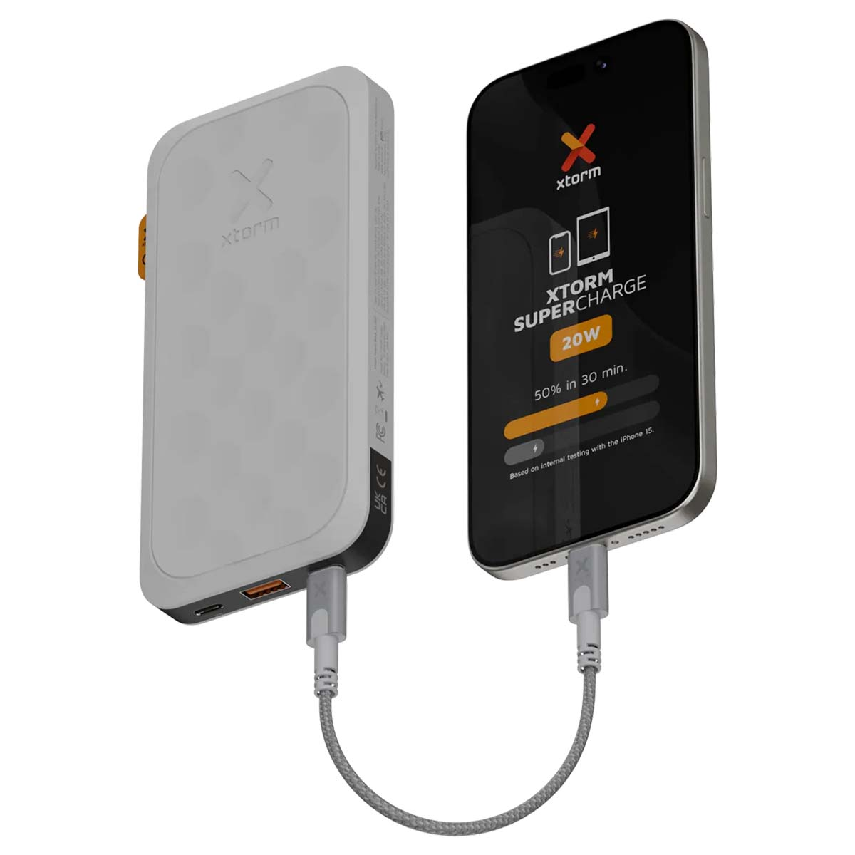 Une power bank Xtorm blanche charge un iPhone 15 via un câble gris.