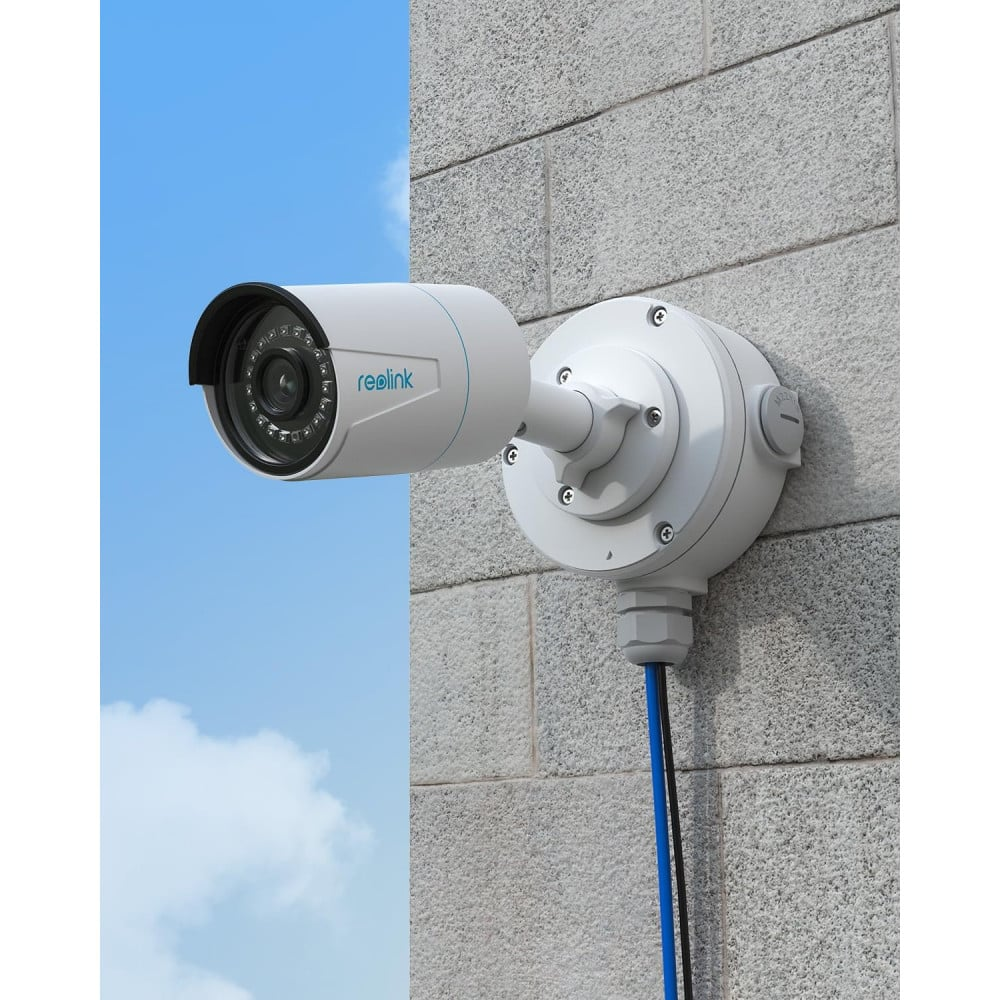 Une caméra de sécurité blanche Reolink montée sur un mur de briques grises sous un ciel bleu.