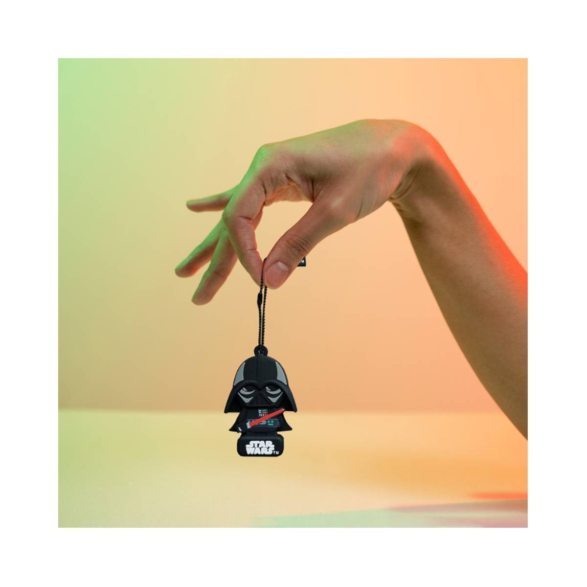 Eine Hand hält einen Darth Vader Anhänger vor einem Farbverlauf von grün zu orange.