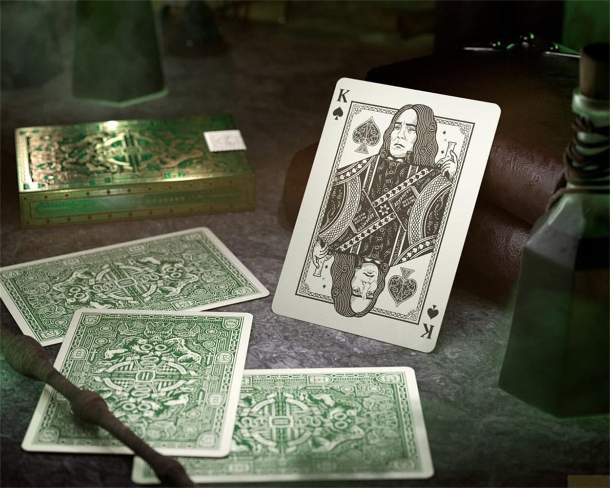 Un jeu de cartes avec boîte verte, carte Roi et dos de cartes sur pierre sombre.