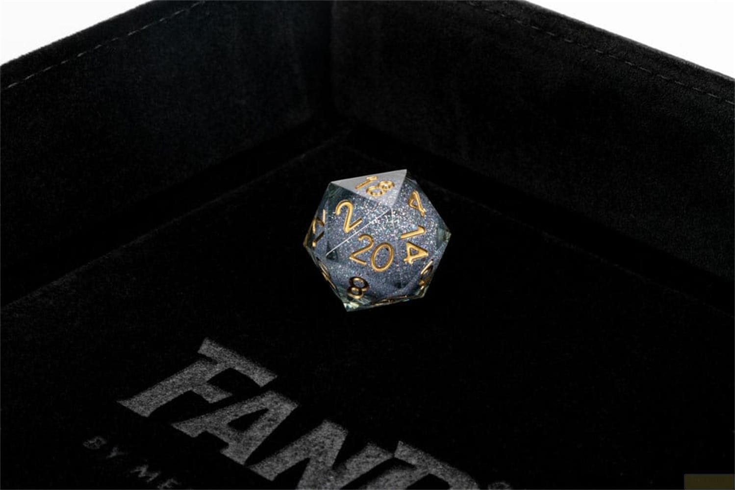 Un dé D20 gris moucheté avec des chiffres dorés repose dans un plateau en velours noir.