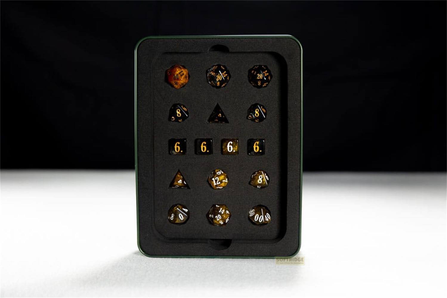 Un ensemble de dés noirs avec numérotation dorée dans un étui en métal.