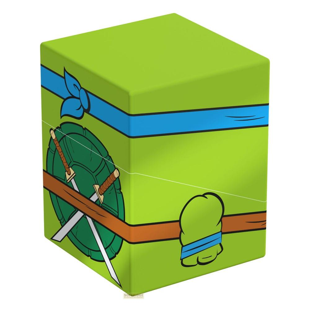 Une boîte verte avec des graphismes TMNT : bouclier, épées, bandana et brassards.