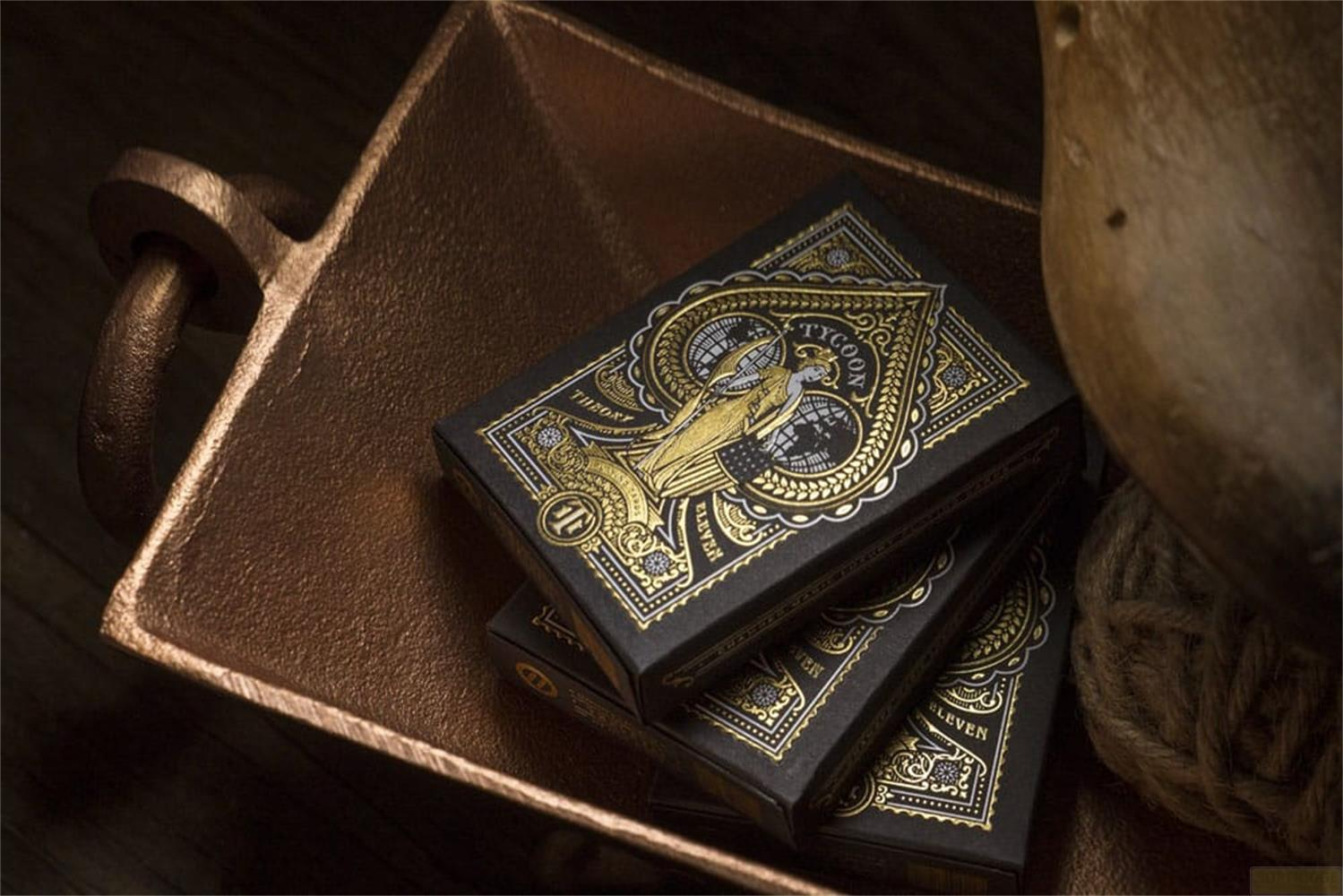 Tre scatole di carte da gioco nere con dettagli dorati in un piatto di rame.