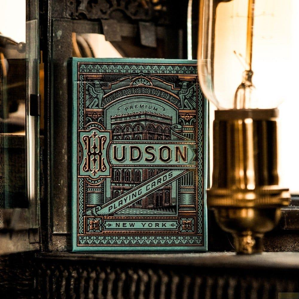 Un cofanetto di carte da gioco con etichetta HUDSON PLAYING CARDS NEW YORK, vicino a una lampadina.