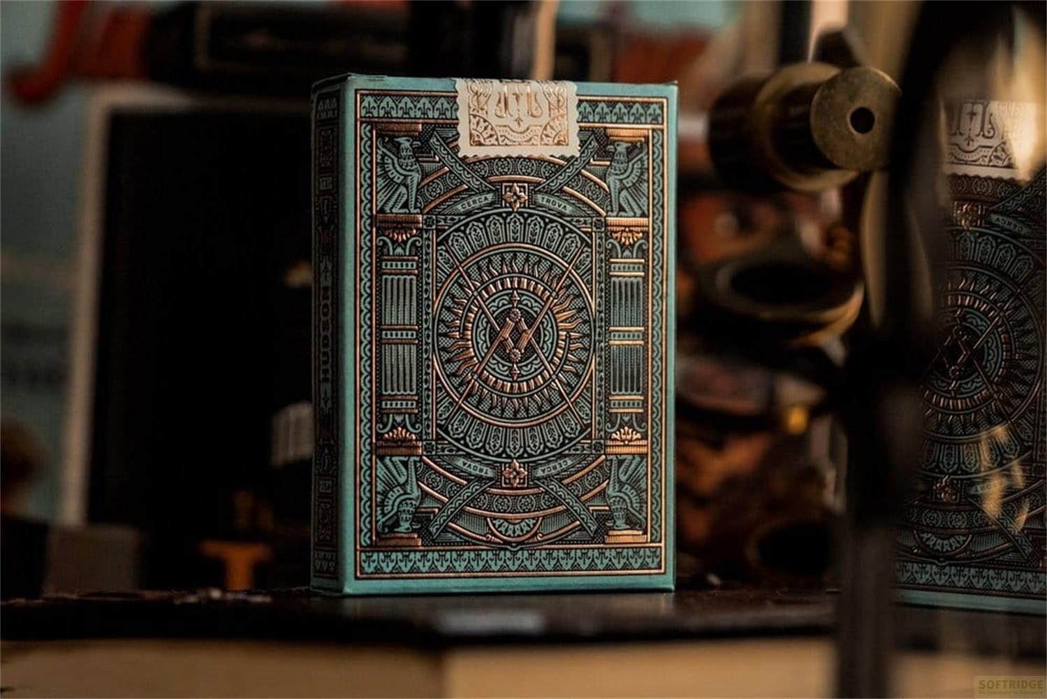 Una scatola di carte da gioco color ottanio con intricati motivi dorati su un tavolo.