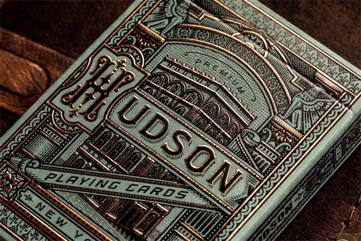 Un primo piano di una scatola di carte da gioco color ottanio e oro, con disegni intricati e la parola "HUDSON".