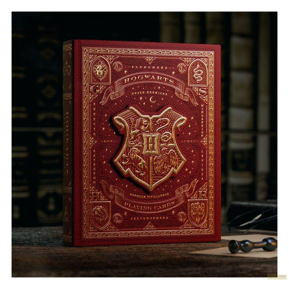 Boîte de jeu de cartes rouge avec blason de Poudlard et ornements dorés sur table en bois.