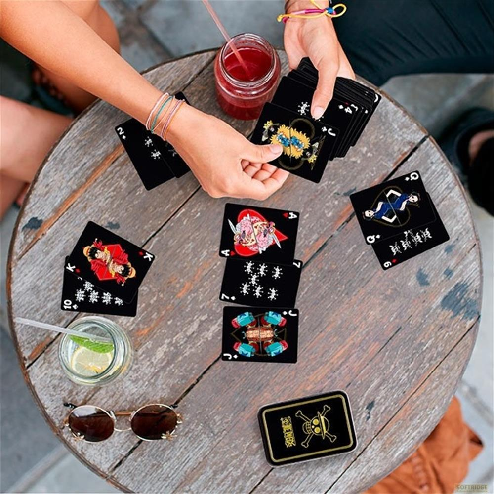 Cartes à jouer noires avec des motifs d'anime sur une table en bois, à côté d'une boisson et de lunettes de soleil.