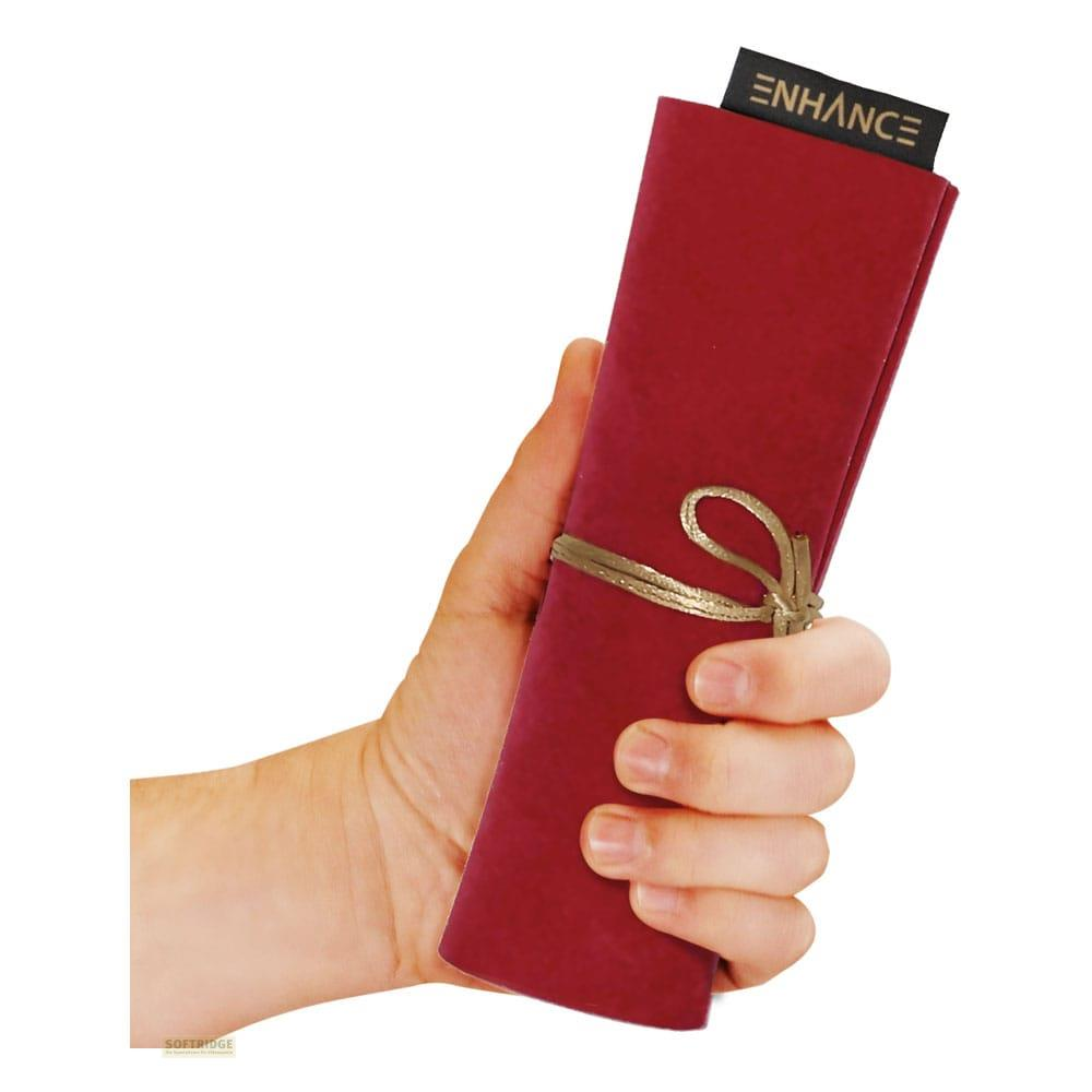 Mano che tiene una custodia arrotolata rosso scuro legata con spago dorato. Logo 'ENHANCE' visibile.