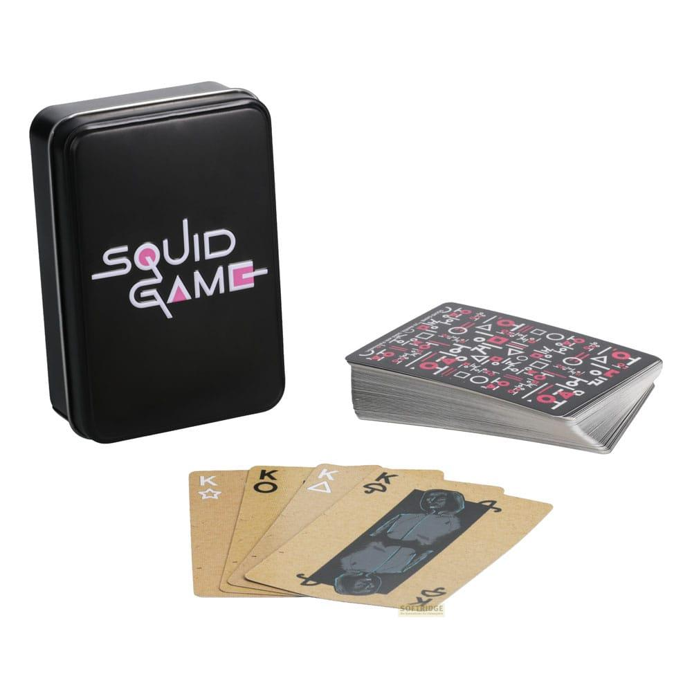 Scatola metallica nera con logo 'Squid Game', mazzo di carte con simboli coreani e quattro re.