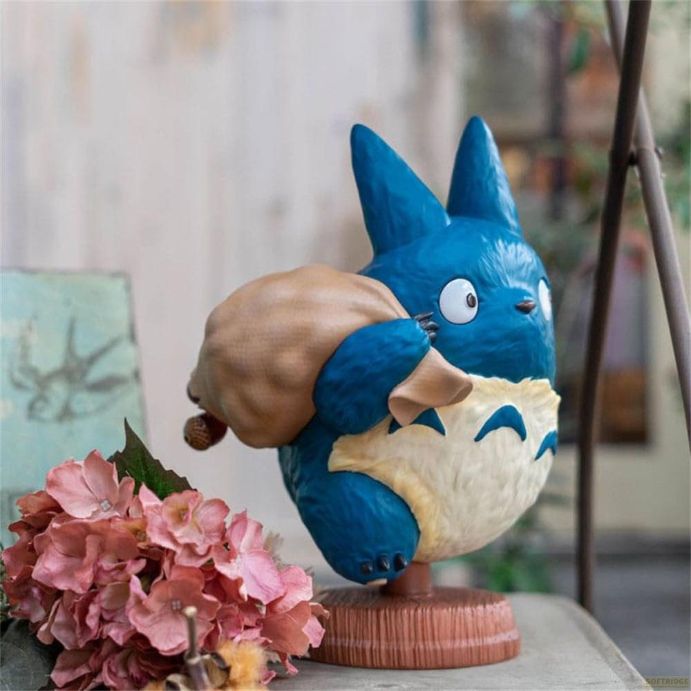Una figura blu di Totoro con un sacco sulla spalla si trova vicino a fiori rosa.