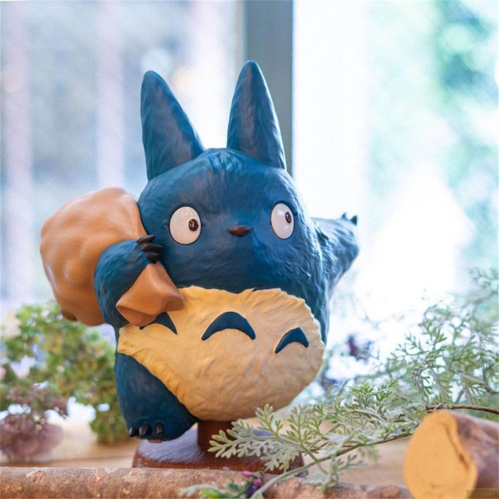 Personaggio blu di Totoro con sacco marrone sulla spalla, davanti alle foglie.