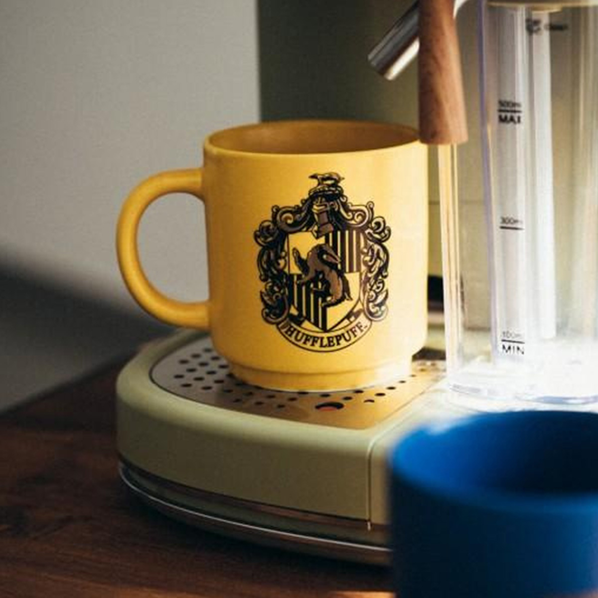 Ein gelber Hufflepuff-Becher steht auf einer Kaffeemaschine neben einem Wasserbehälter.