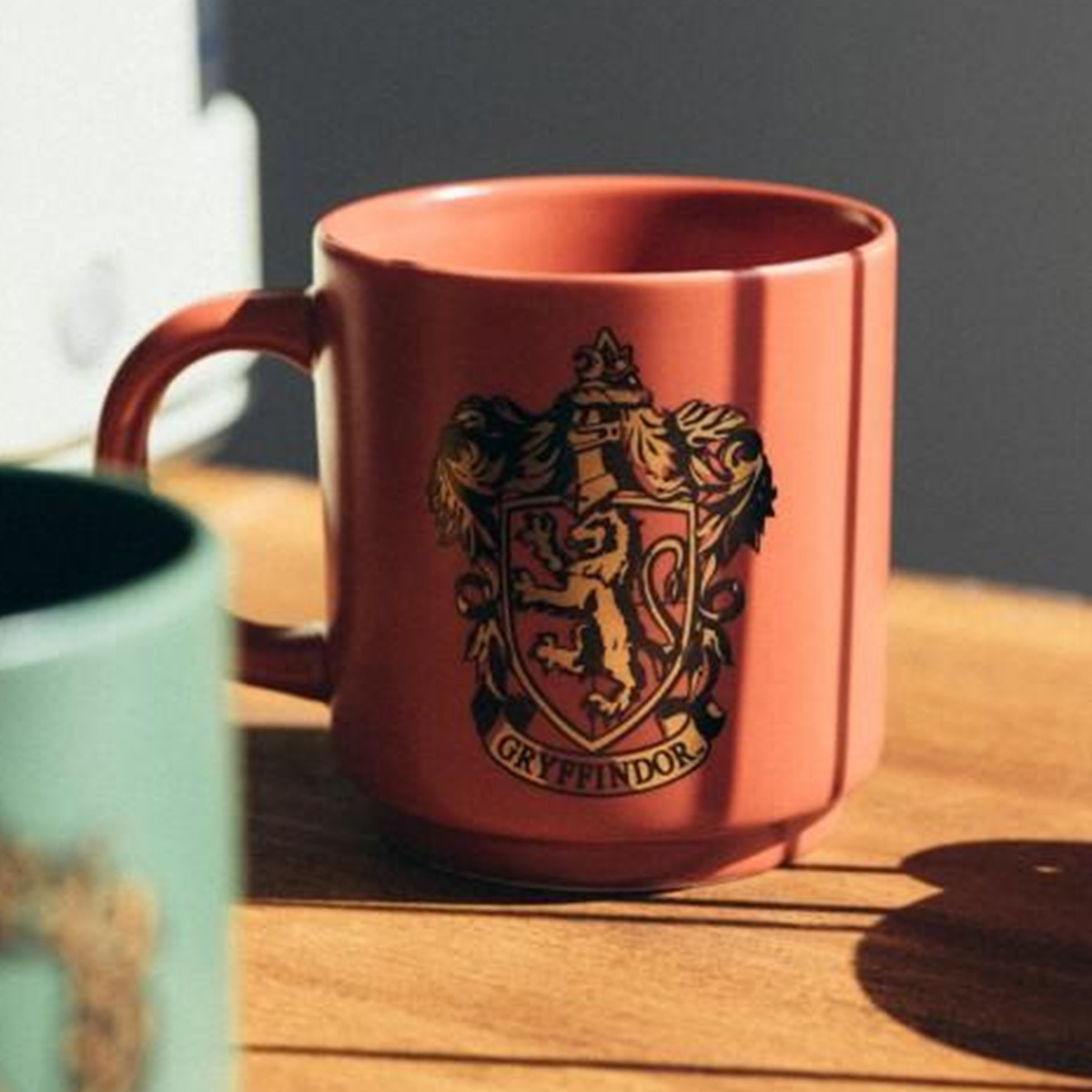 Eine korallenfarbene Tasse mit dem Gryffindor-Wappen und dem Text GRYFFINDOR.
