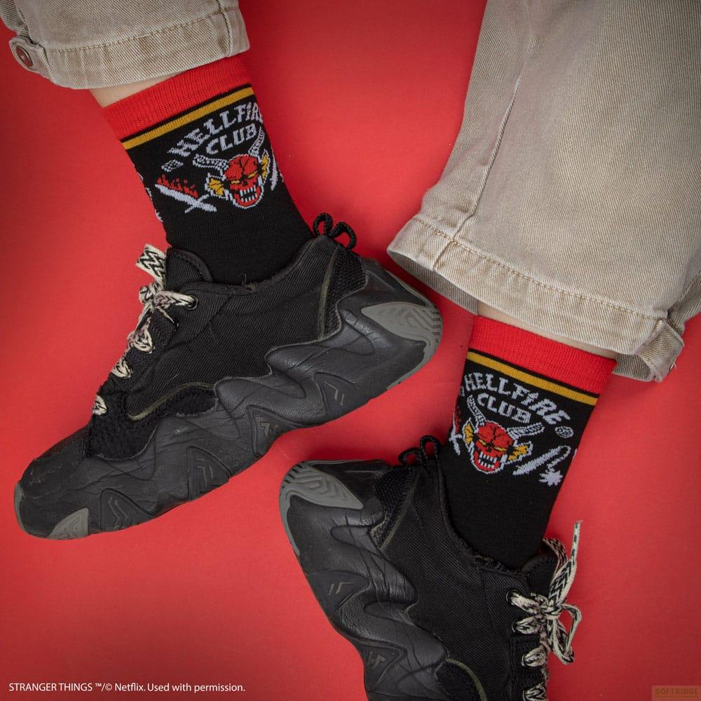 Baskets noires et chaussettes noires avec bords rouges arborant le logo 'Hellfire Club' sur fond rouge.