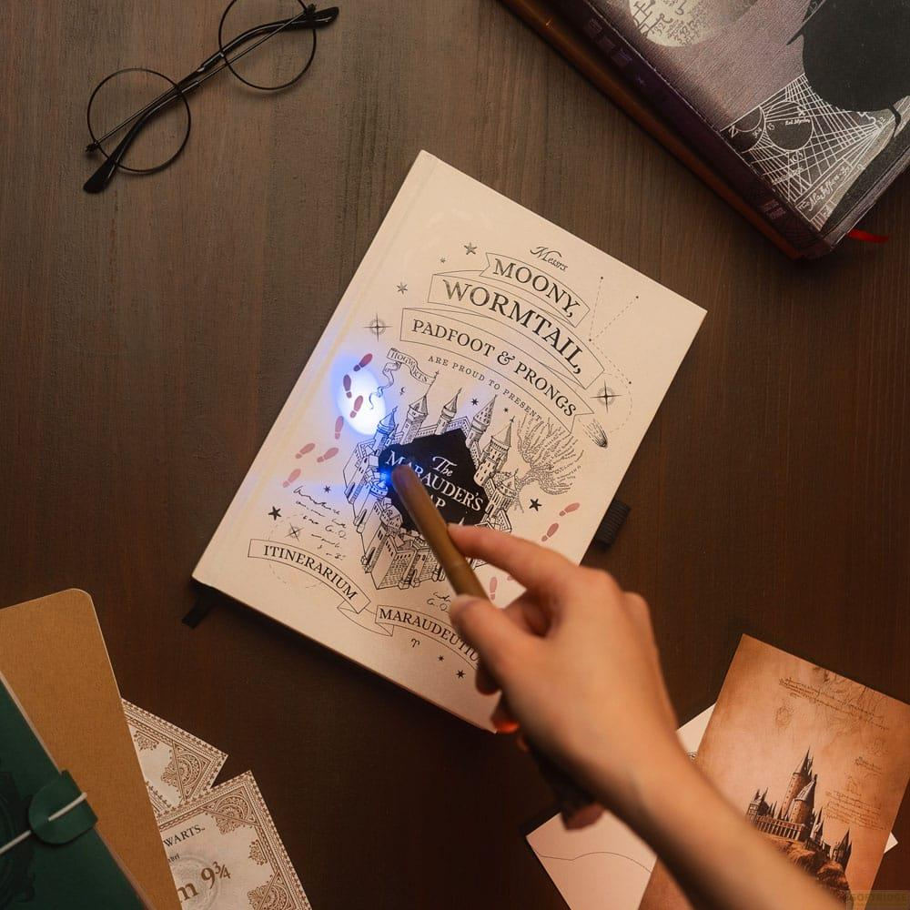 Mano sostiene varita sobre libro Mapa del Merodeador, revela huellas. Gafas cerca.