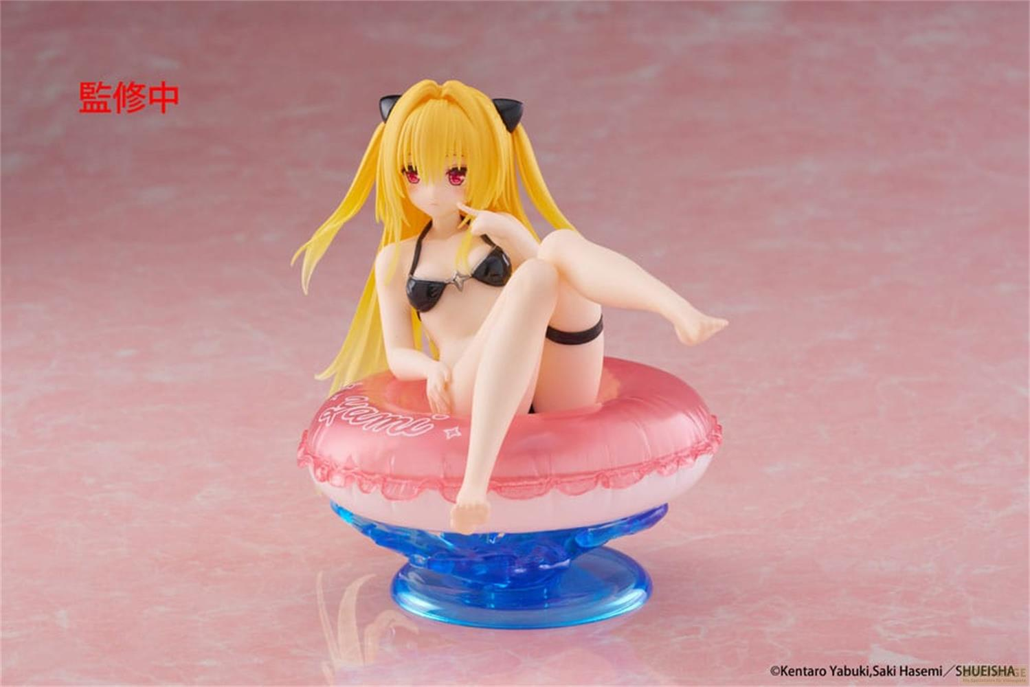 Eine Figur mit gelben Haaren und schwarzem Bikini sitzt in einem rosa Schwimmring auf einem blauen Sockel.