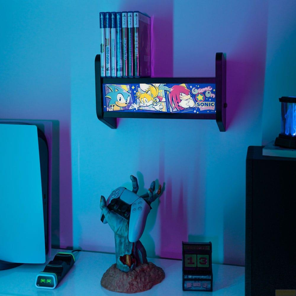 Un estante con juegos, personajes de Sonic y un soporte para mando con PS5.