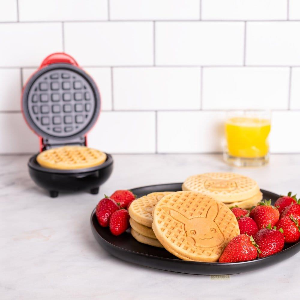 Ein roter Mini-Waffelmaker mit Waffel; Waffeln und Erdbeeren auf schwarzer Platte.