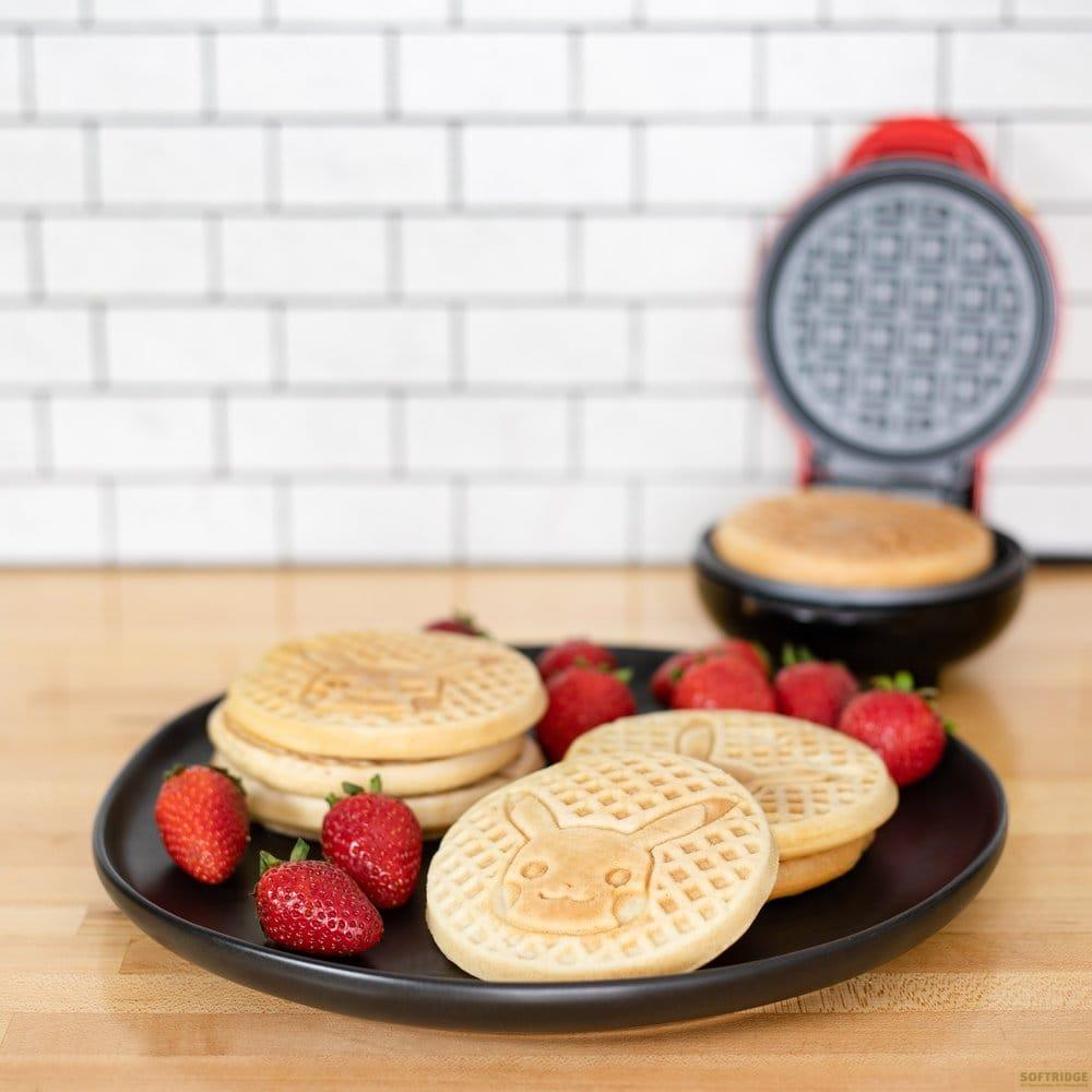 Pikachu-Waffeln mit Erdbeeren auf schwarzer Platte neben einem offenen Waffeleisen.