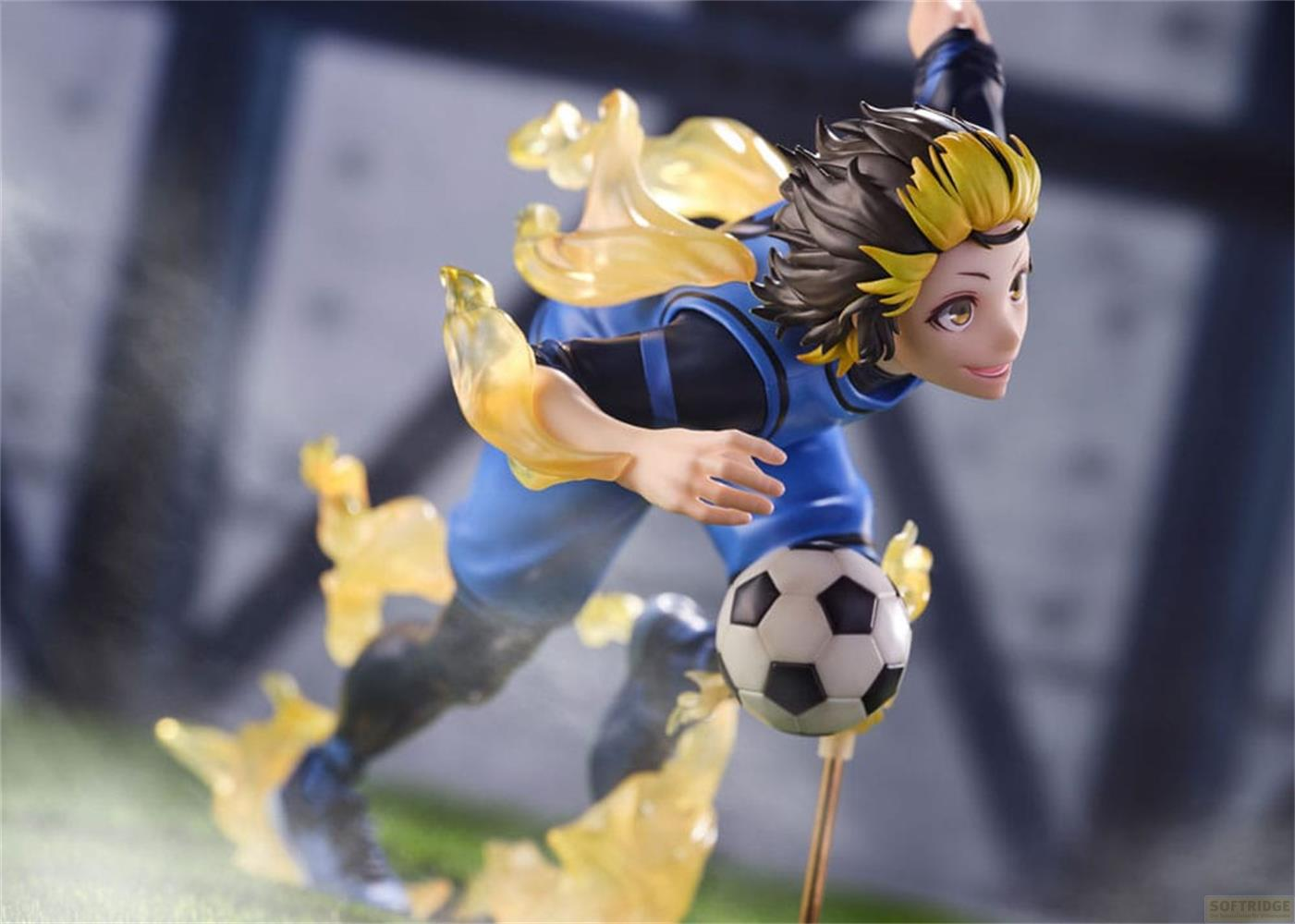 Figura de anime de futbolista con uniforme azul y llamas amarillas, pateando un balón.