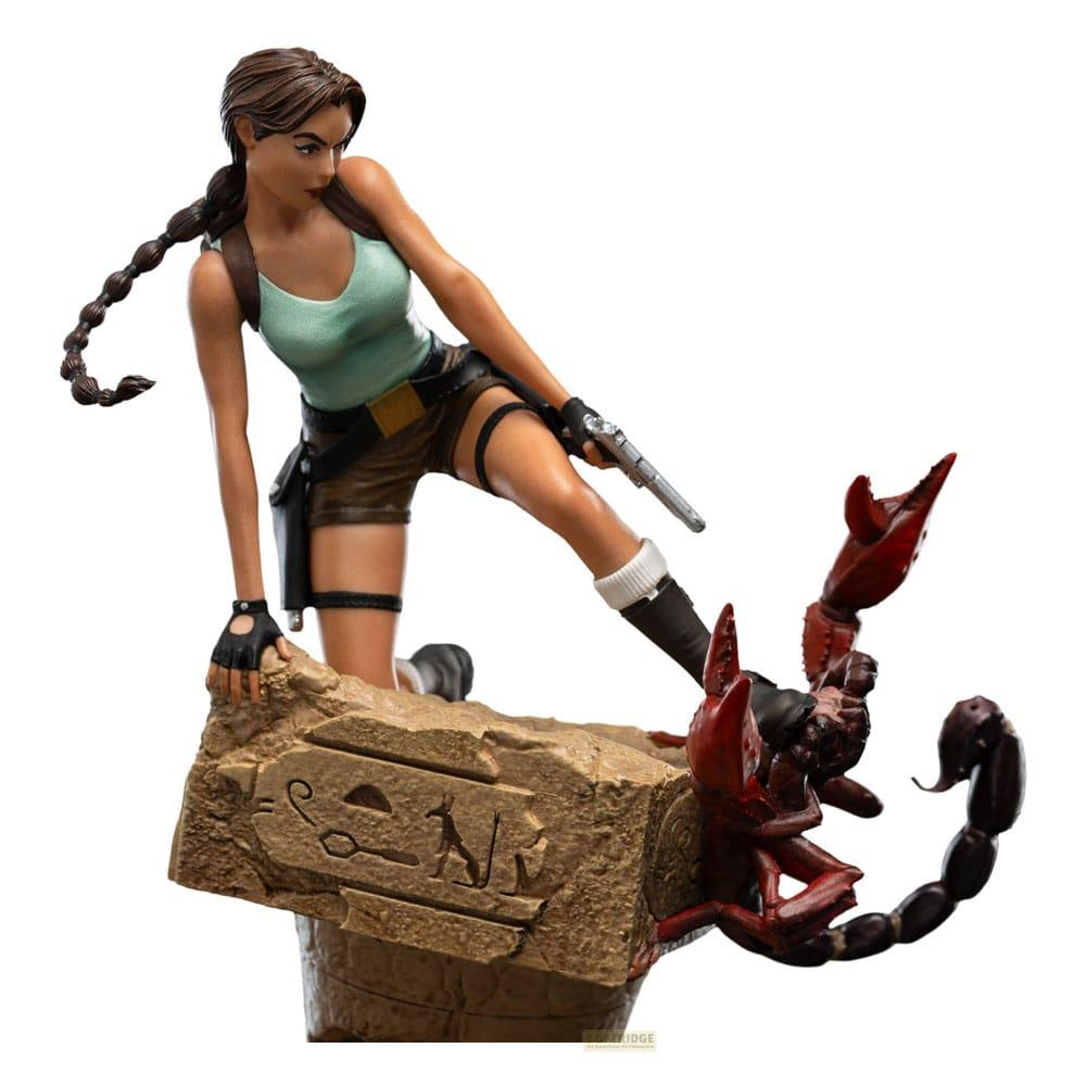 Lara Croft mit Waffe steht auf Felsen neben rotem Skorpion.