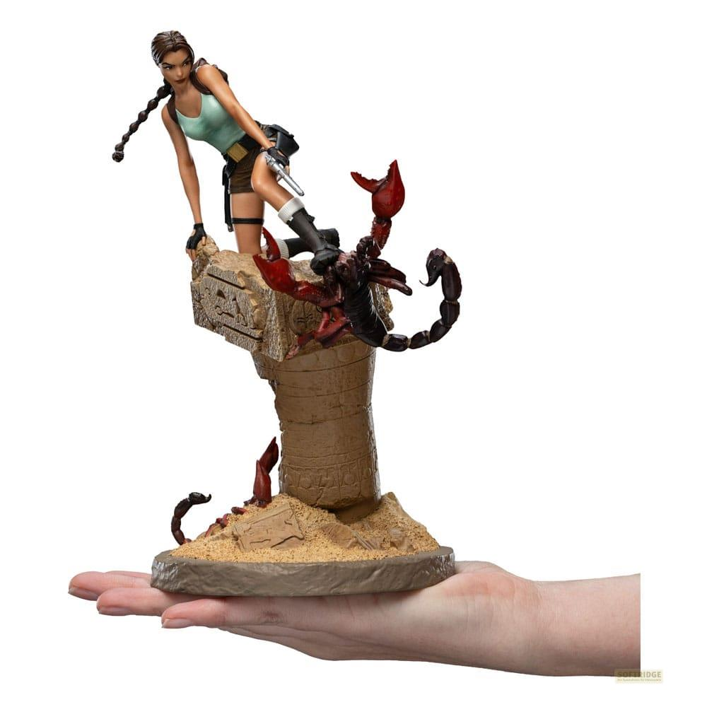 Lara Croft Figur mit Skorpion auf ruinösem Sockel, gehalten von einer Hand.