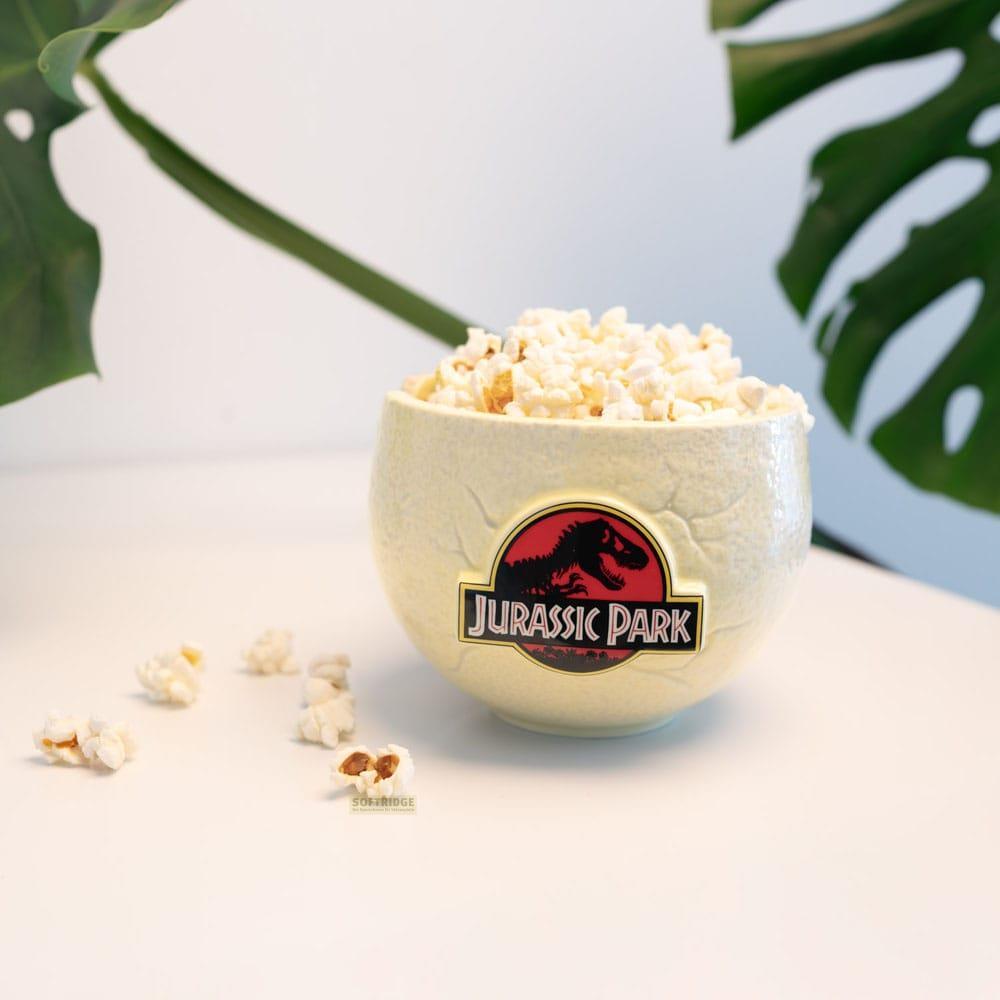 Un cuenco amarillo con logo de Jurassic Park, lleno de palomitas. Algunas palomitas esparcidas cerca.