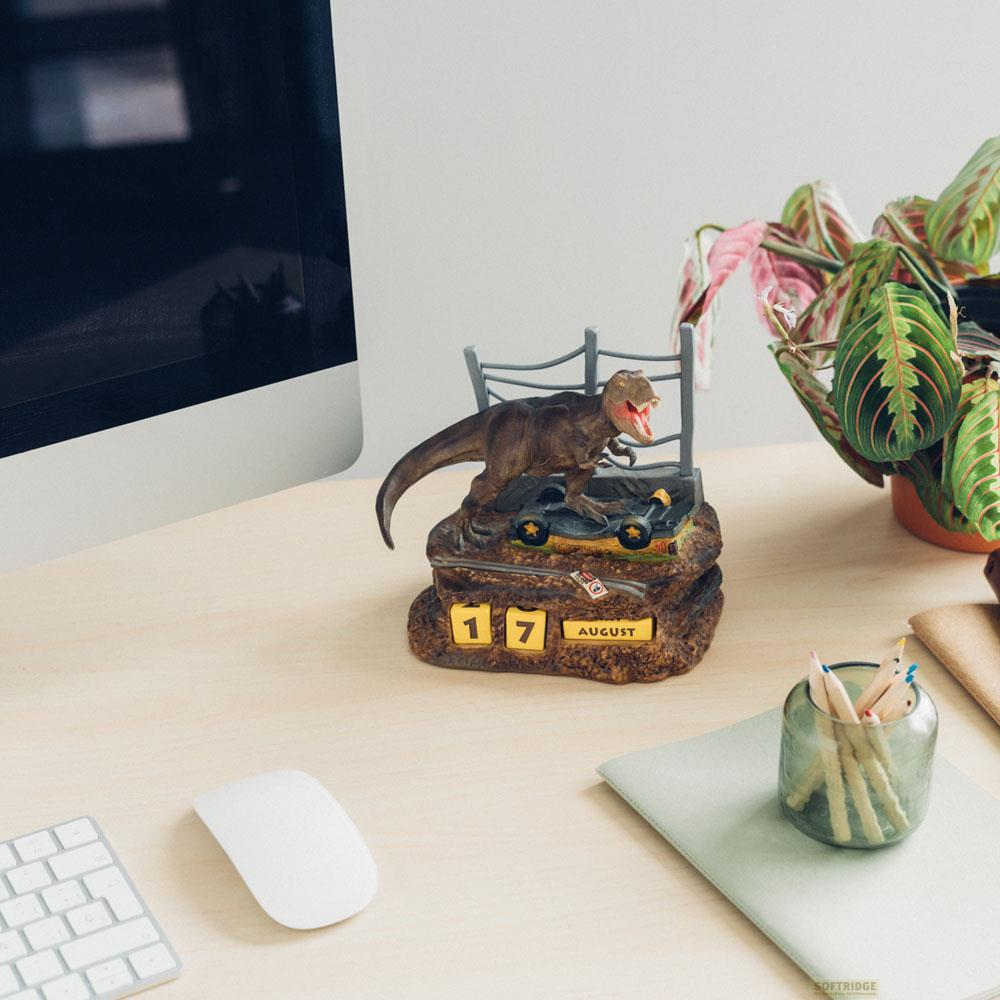 Un calendario de T-Rex en un escritorio, con una computadora y una planta.