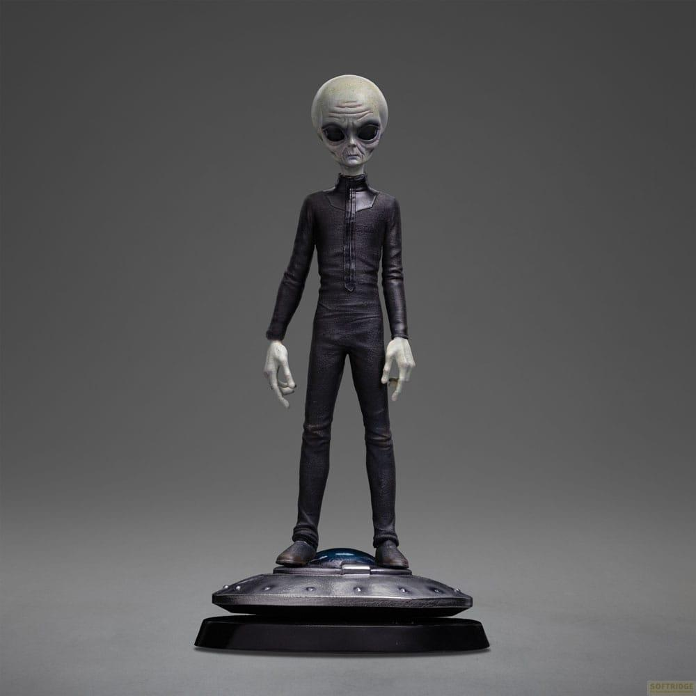 Una figura aliena grigia in abito nero sta su una base UFO.
