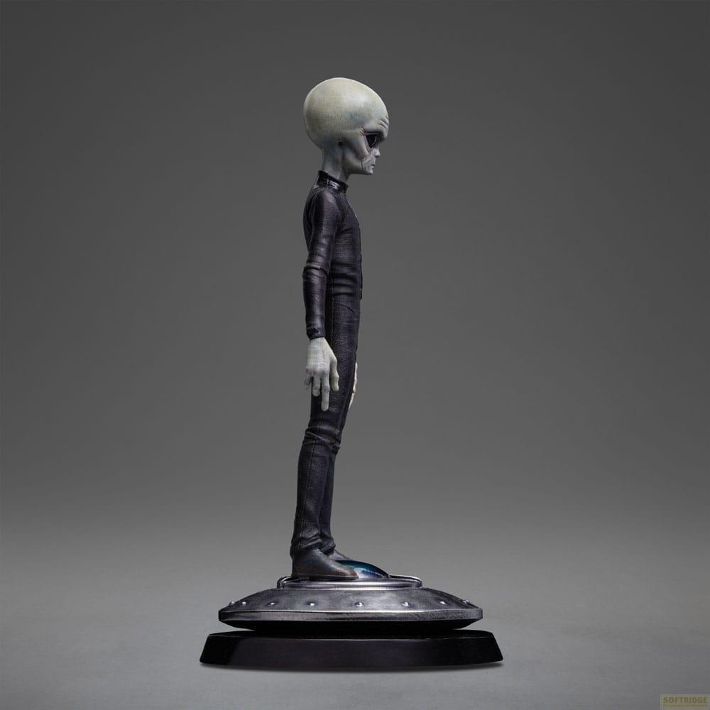 Una figura aliena grigia in abito nero su una base a forma di disco.