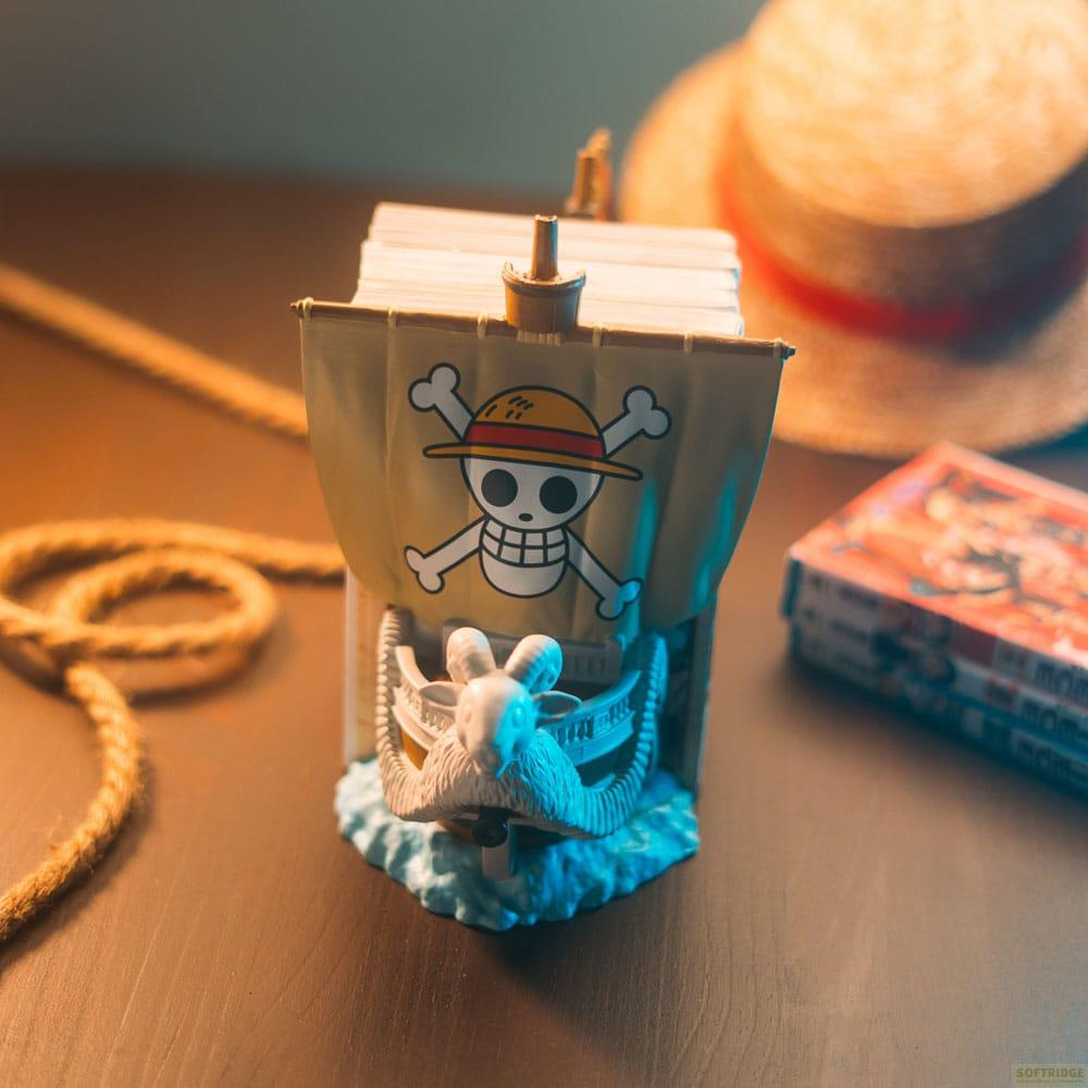 Un modelo de barco con bandera Jolly Roger, cuerda y sombrero en mesa.