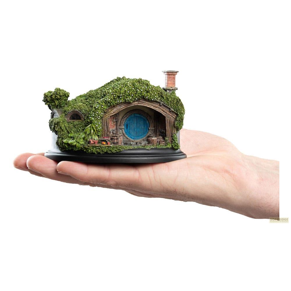 Ein Hobbit-Hausmodell mit runder blauer Tür und Schornstein liegt in einer Hand.