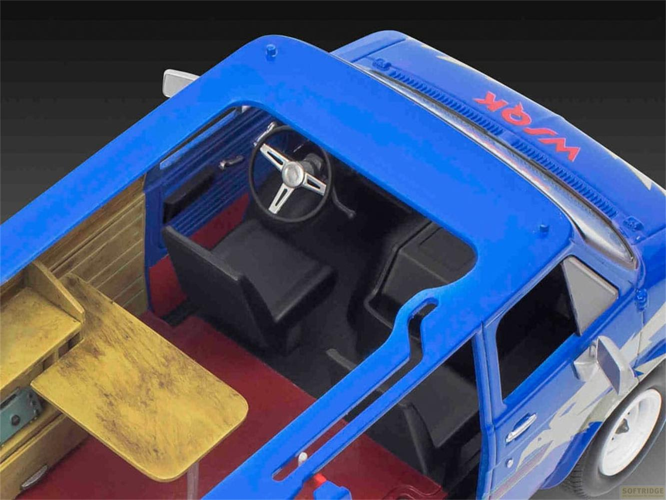 Voiture modèle bleue avec table en bois, sièges noirs et tapis rouge.