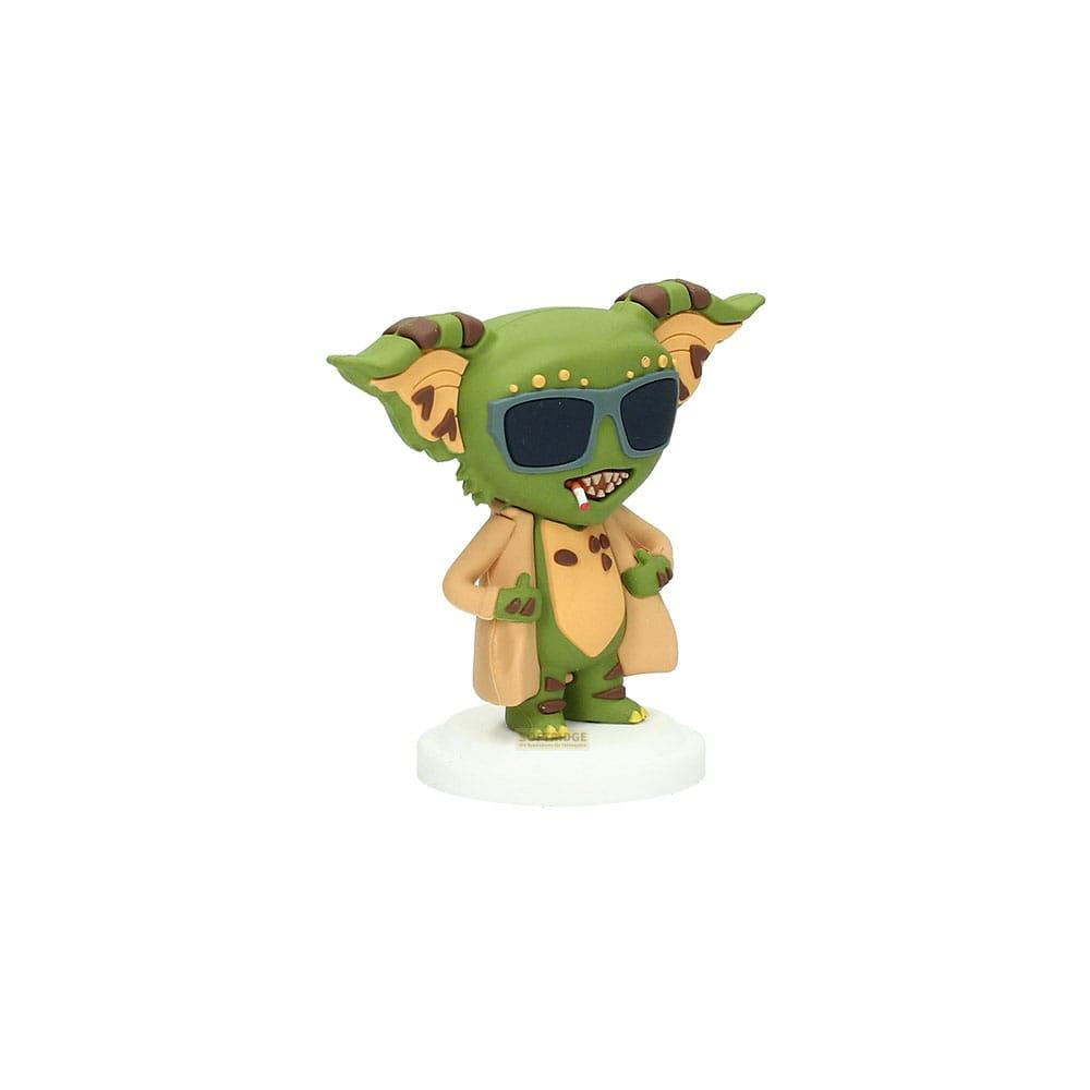 Una figura de gremlin verde con gafas de sol y abrigo color canela sobre base blanca.